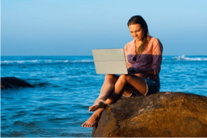 A person sitting on a rock with a computer
